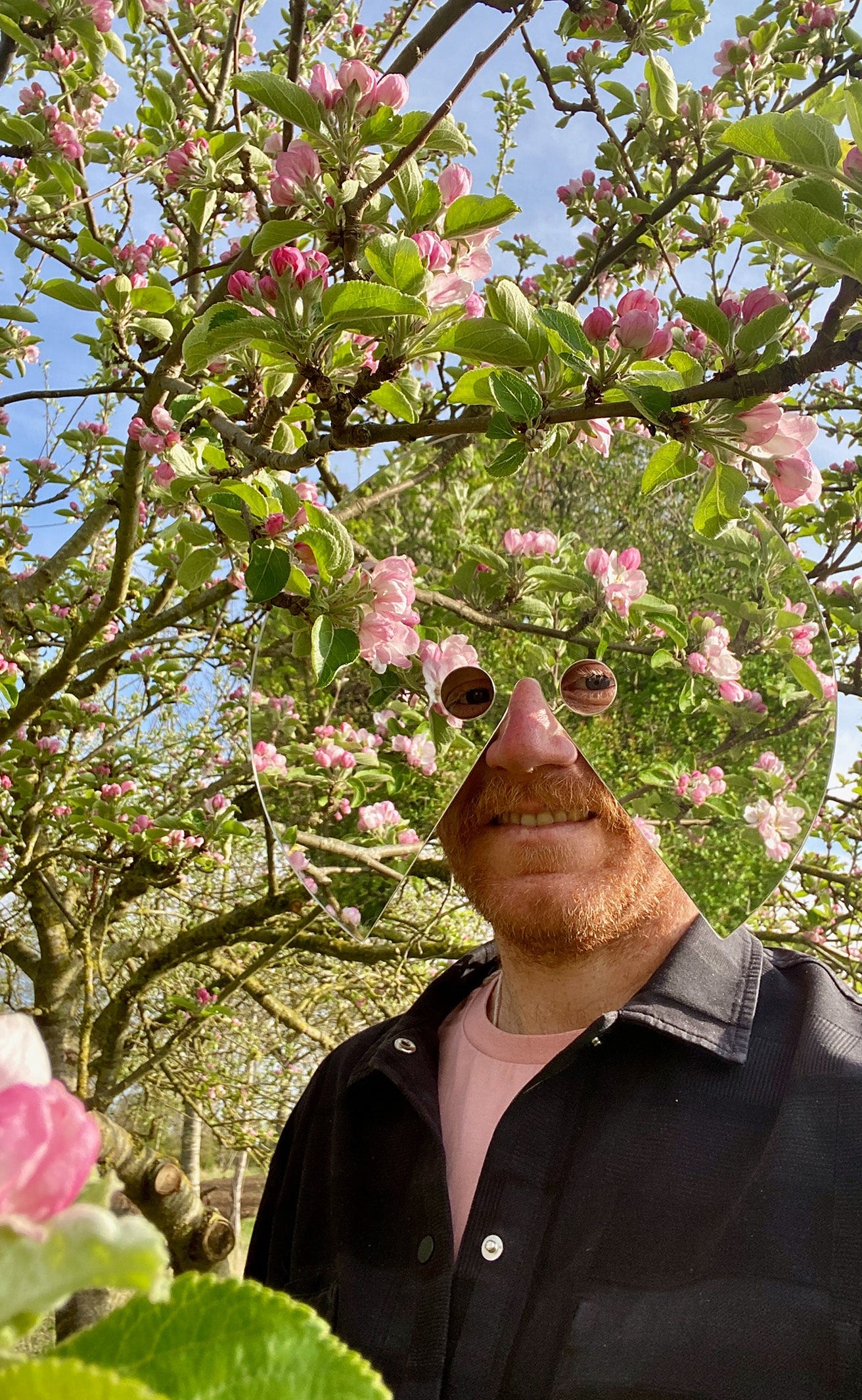 Person wearing a mask with a flower-like design in an apple orchard.